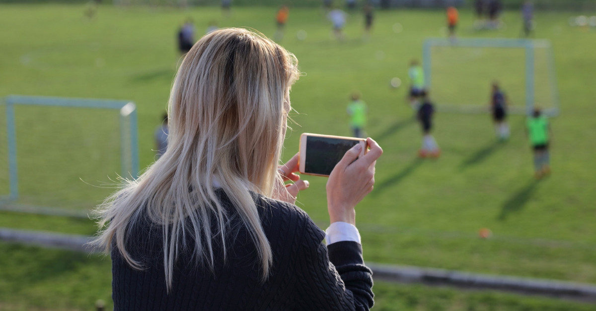 mother recording youth sports game on phone